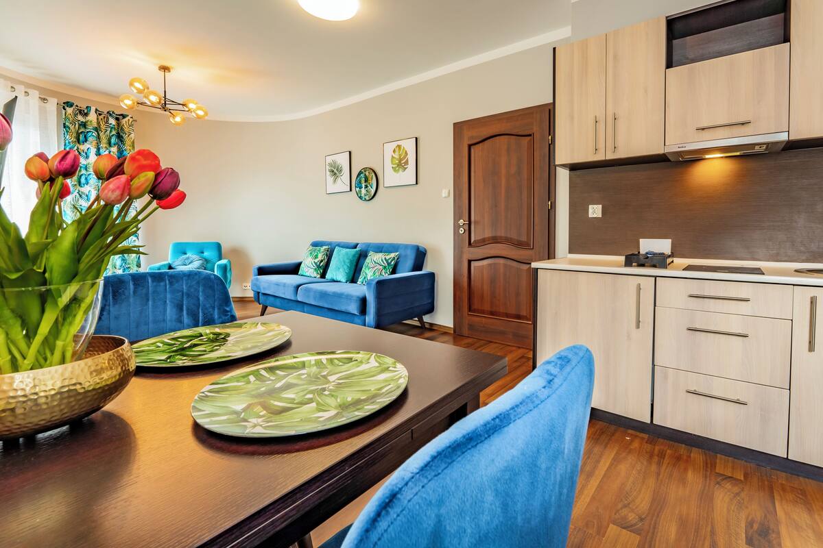 Una cocina moderna con armarios de madera, una mesa de comedor con un jarrón de tulipanes y un sofá azul en la sala de estar.