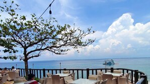 Une terrasse en bois avec des sièges extérieurs, un arbre et une vue sur la mer.