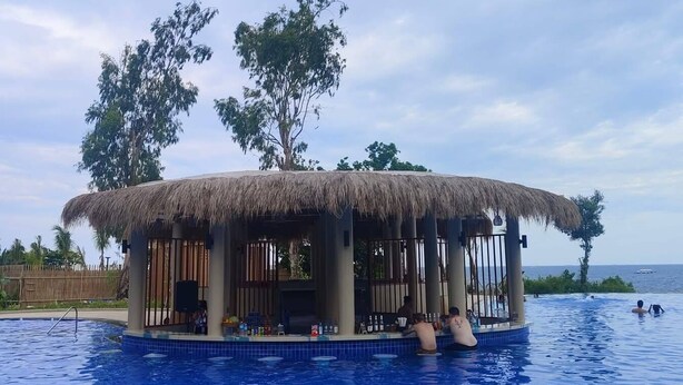 Une structure à toit de chaume surplombant une piscine, offrant une vue dégagée sur l’océan.