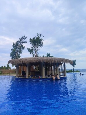 Une structure à toit de chaume surplombant une piscine, offrant une vue dégagée sur l’océan.