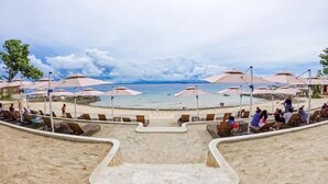 Un complexe hôtelier situé en bord de mer, doté de chaises longues et de parasols, d’une piscine et offrant une vue sur l’océan.