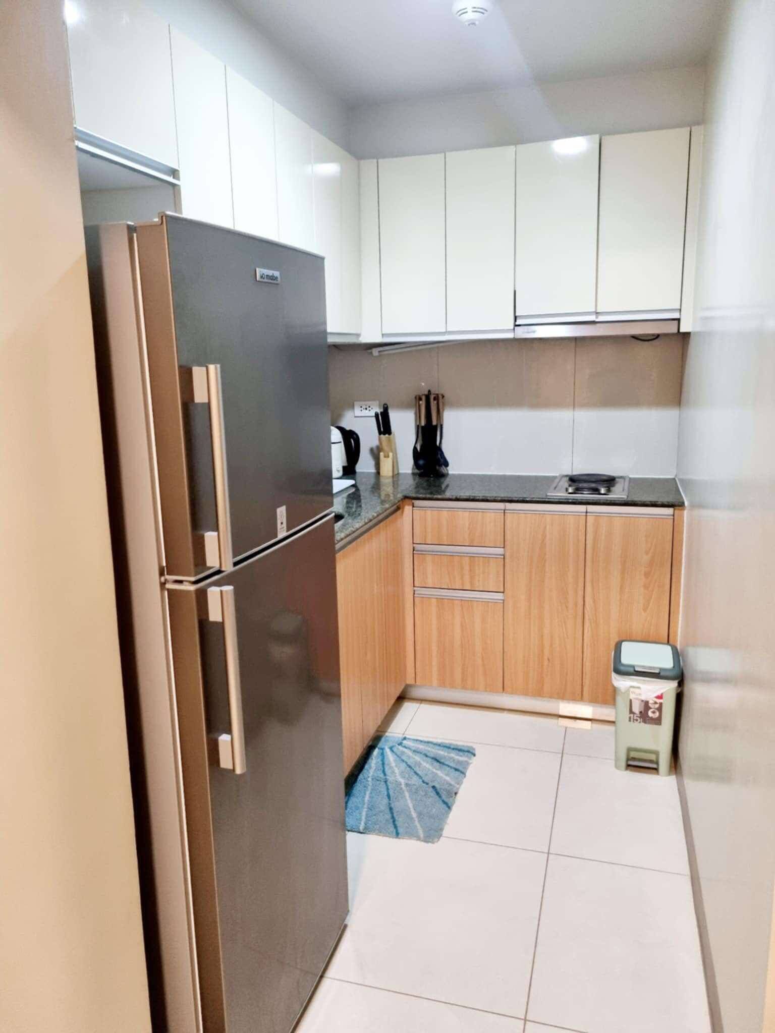 Una cocina compacta con un refrigerador de acero inoxidable, armarios de madera, una pequeña encimera y un cubo de basura.