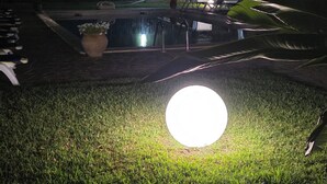 A well-lit outdoor area with a lawn, a large circular light, and a vehicle parked nearby. - Penta Dream House Prince (Sicilia)
