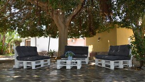 A patio with three white wooden chairs and a matching table, surrounded by a stone floor and shaded by a tree. - Penta Dream House Prince (Sicilia)
