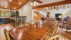 Un vaste espace à manger avec une grande table et des chaises en bois, un ventilateur de plafond et un escalier menant à un niveau supérieur.