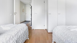 A minimalist bedroom with two beds, a wardrobe, and a hallway leading to another room. - Kotimaailma KotikaksioKirkkok (Lahti)
