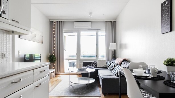A modern apartment with a kitchen, dining area, and living room. It features a large window, a ceiling fan, and a wall-mounted air conditioner. - Kotimaailma KotikaksioKirkkok (Lahti)