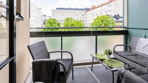 A balcony with wicker furniture, a small table with a plant, and a view of city buildings and trees. - Kotimaailma KotikaksioKirkkok (Lahti)