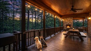 Une terrasse en bois avec une cheminée en pierre, des sièges d’extérieur et une vue sur une zone boisée.