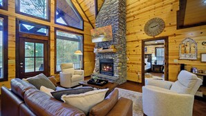 Un intérieur de chalet chaleureux avec une cheminée en pierre, des canapés en cuir et de grandes fenêtres.