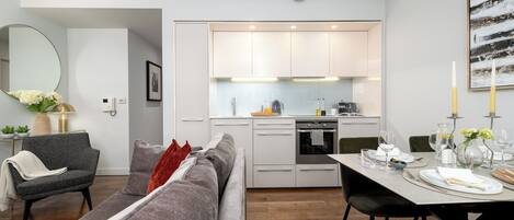 A modern kitchen with white cabinets, a built-in oven, and a dining area with a table set for two.