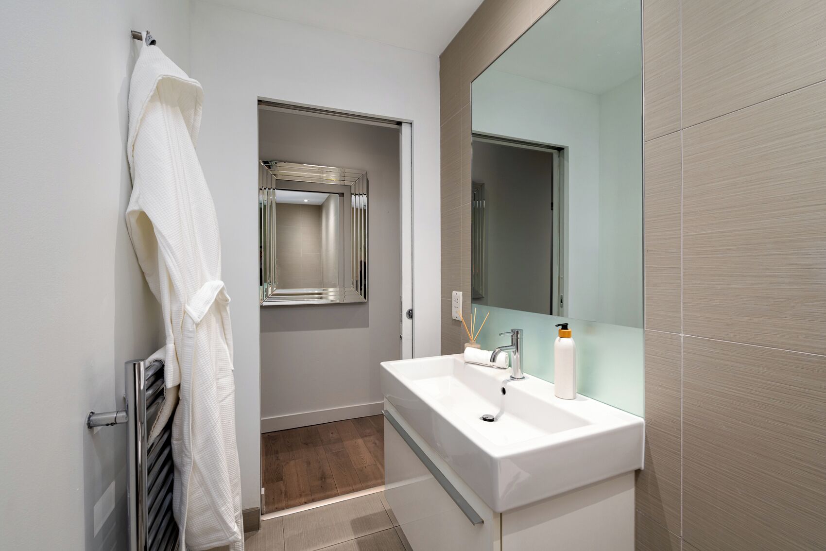 Une salle de bain moderne avec un lavabo blanc, un miroir et une serviette suspendue à un porte-serviettes.