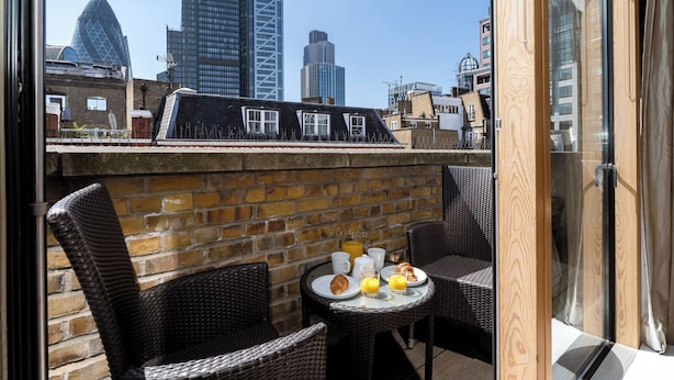 A rooftop terrace with wicker furniture, a brick wall, and a table set for breakfast. - Your Apartment - Liverpool Street (London)