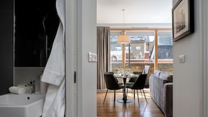 A modern bathroom with a sink, towel, and shower. It leads to a dining area with a table, chairs, and a view of the city. - Your Apartment - Liverpool Street (London)