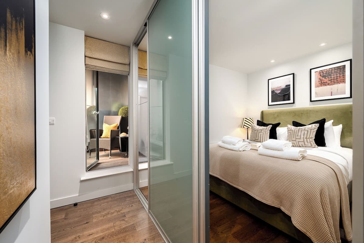 A modern hotel room with a glass partition, a bed with neatly folded towels, and two framed pictures on the wall.