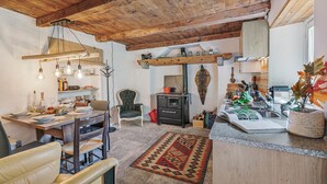 Une cuisine rustique avec des poutres en bois, un coin repas avec des chaises en cuir et un îlot de cuisine doté d’un évier et d’objets décoratifs.