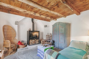 A cozy room with a wooden ceiling, a fireplace, a wicker chair, a bed, and a blue cabinet. - Casa Kaia Verzasca (Sonogno)