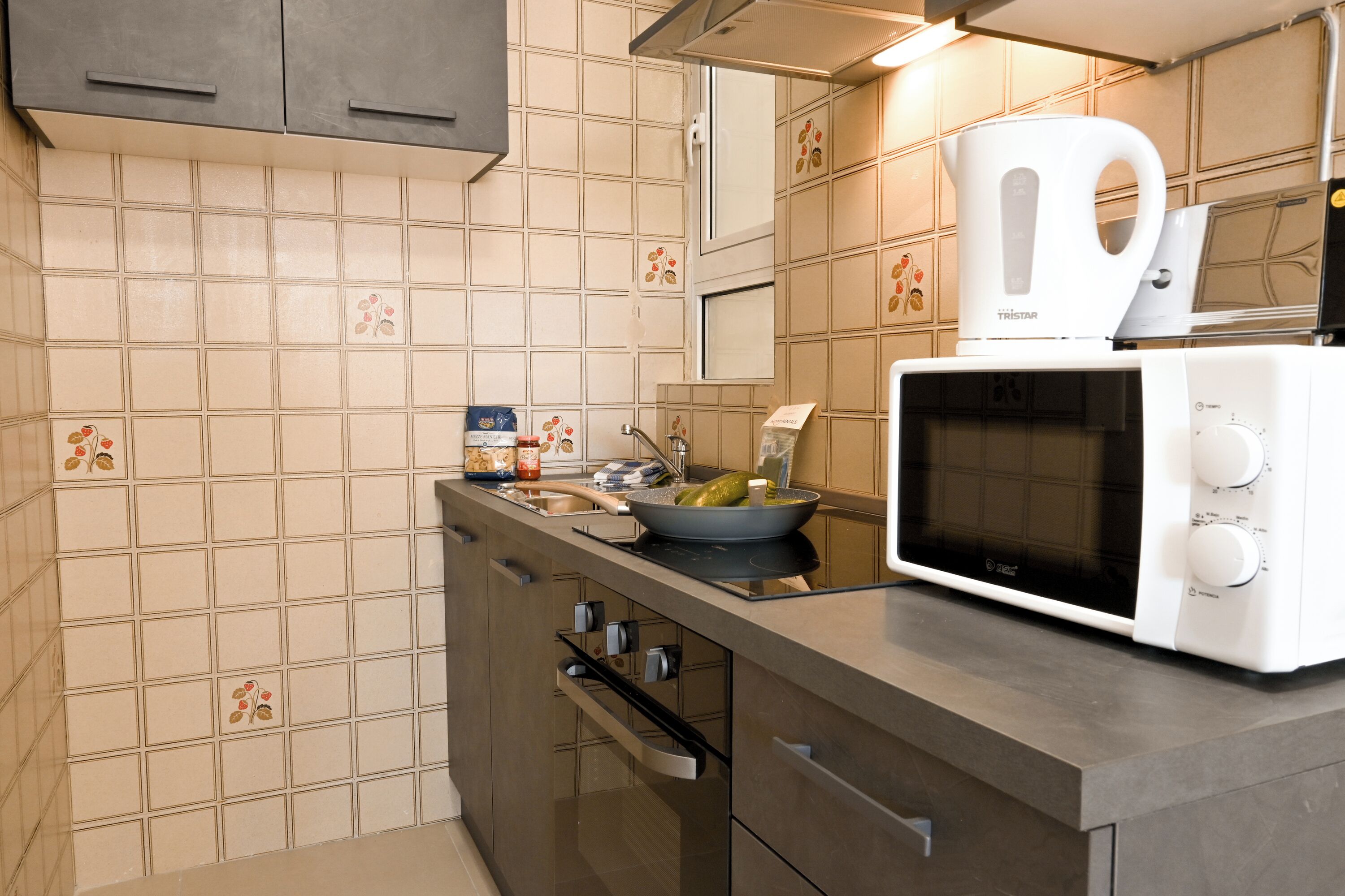 Cocina moderna con microondas, tetera y un tazón de pepinillos en la encimera.