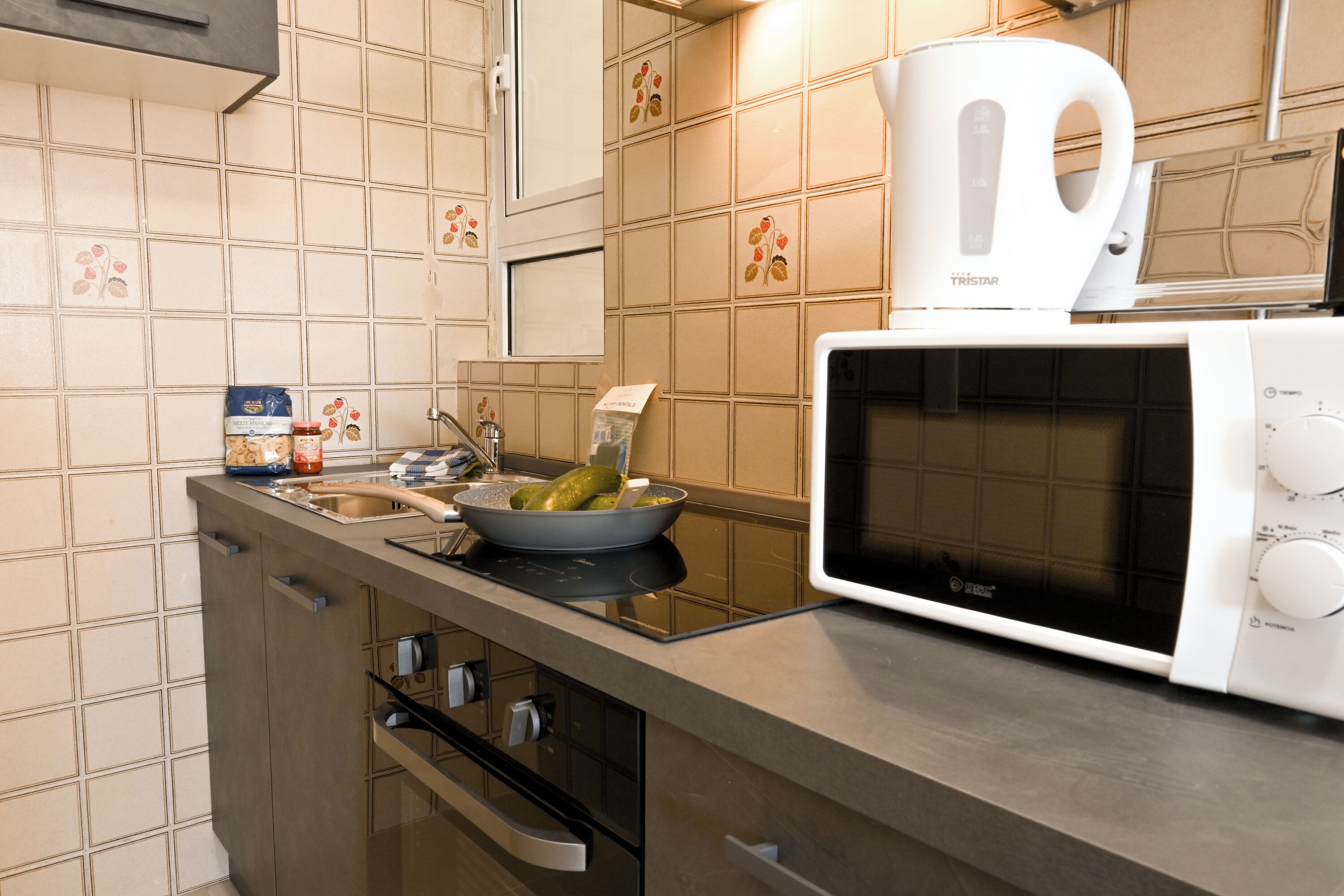Een keuken met een magnetron, waterkoker, spoelbak en een schaal augurken.