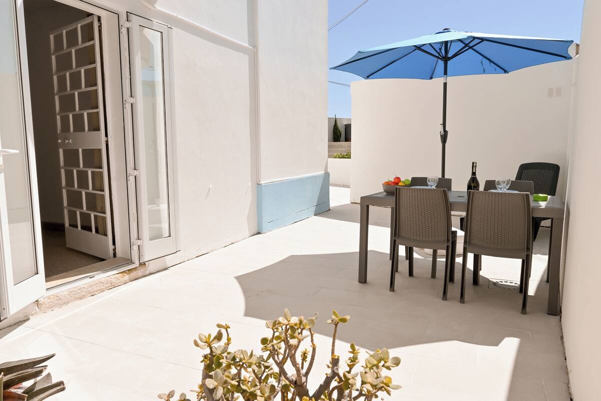 An outdoor patio with a table, chairs, and a blue umbrella.