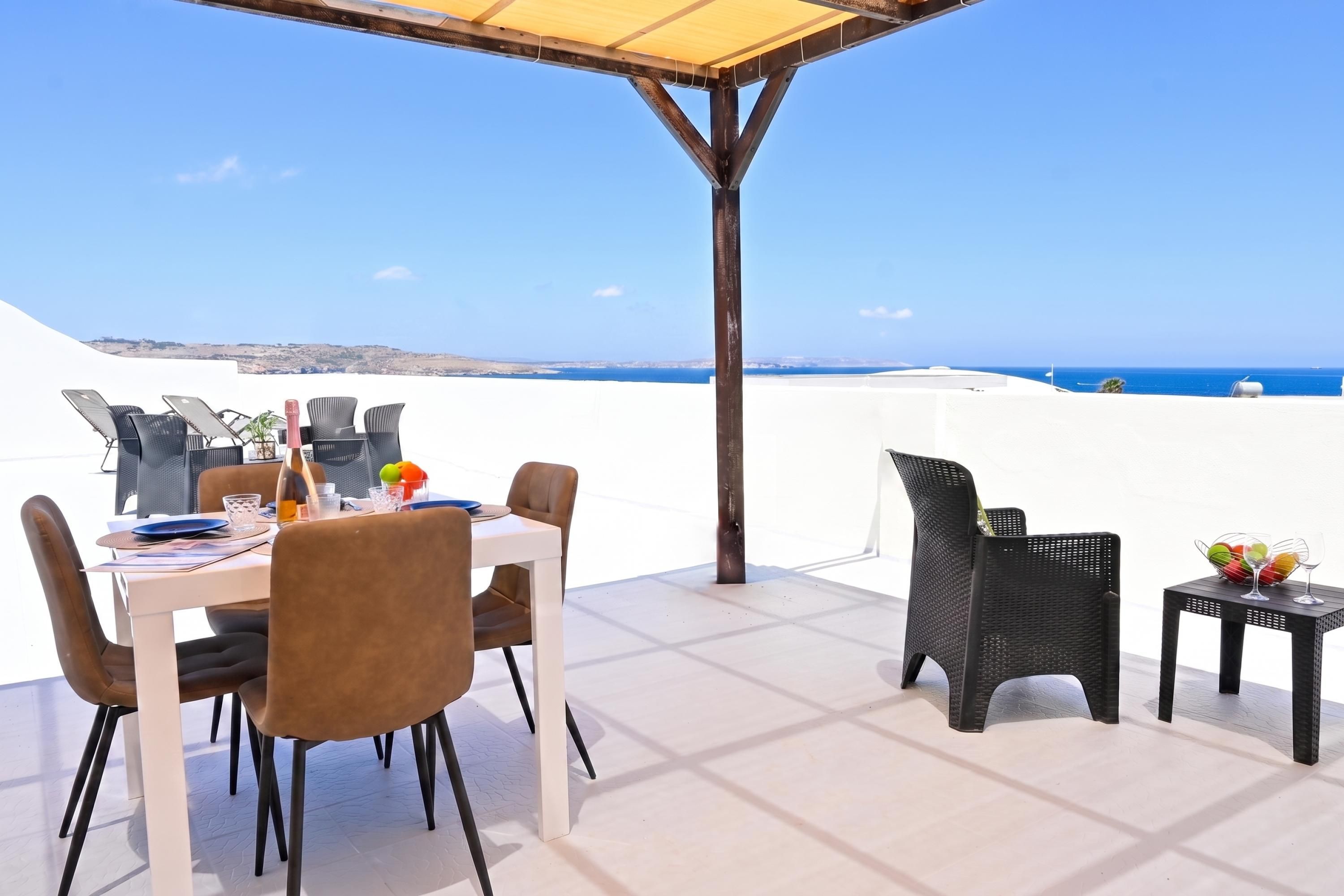 An outdoor dining area with a table set for two, chairs, and a view of the sea.