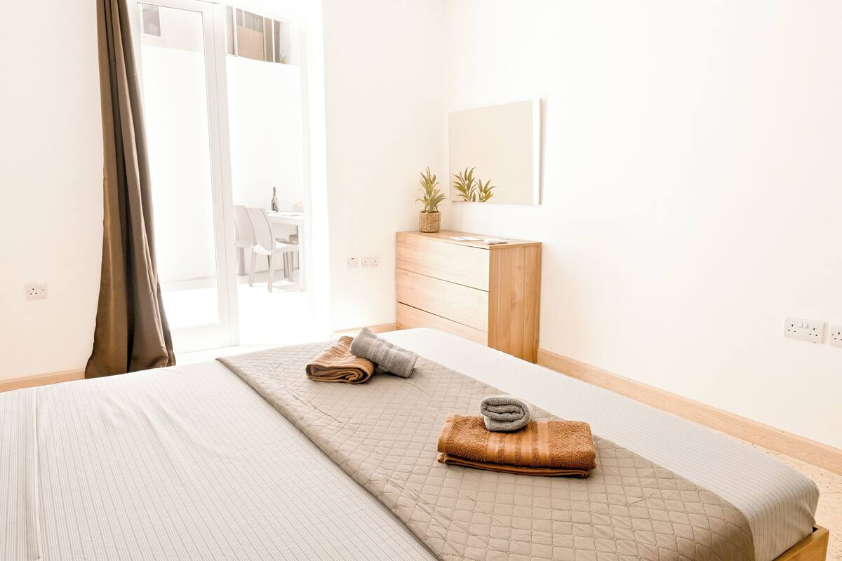A bedroom with a bed, a dresser, a mirror, and a window with curtains.