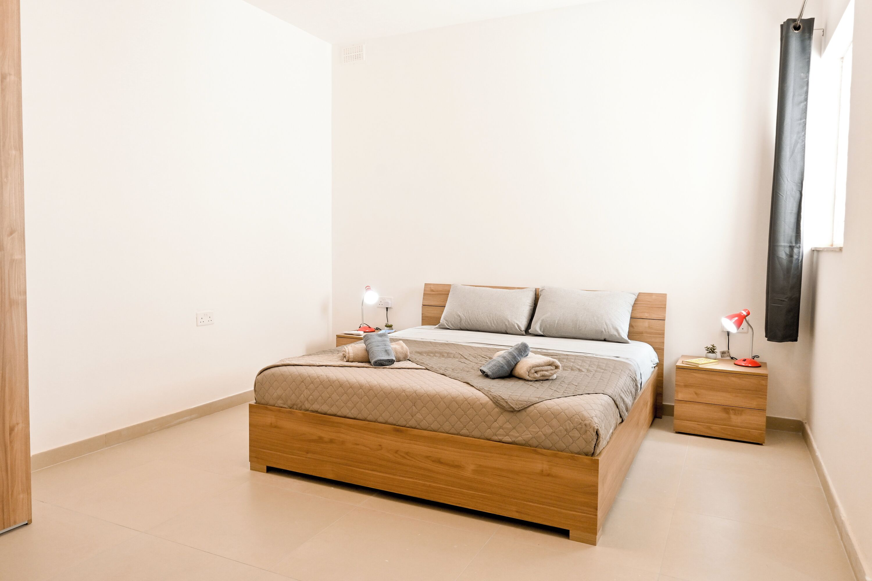 A neatly made bed with a wooden frame, a bedside table with a lamp, and a wall-mounted curtain.