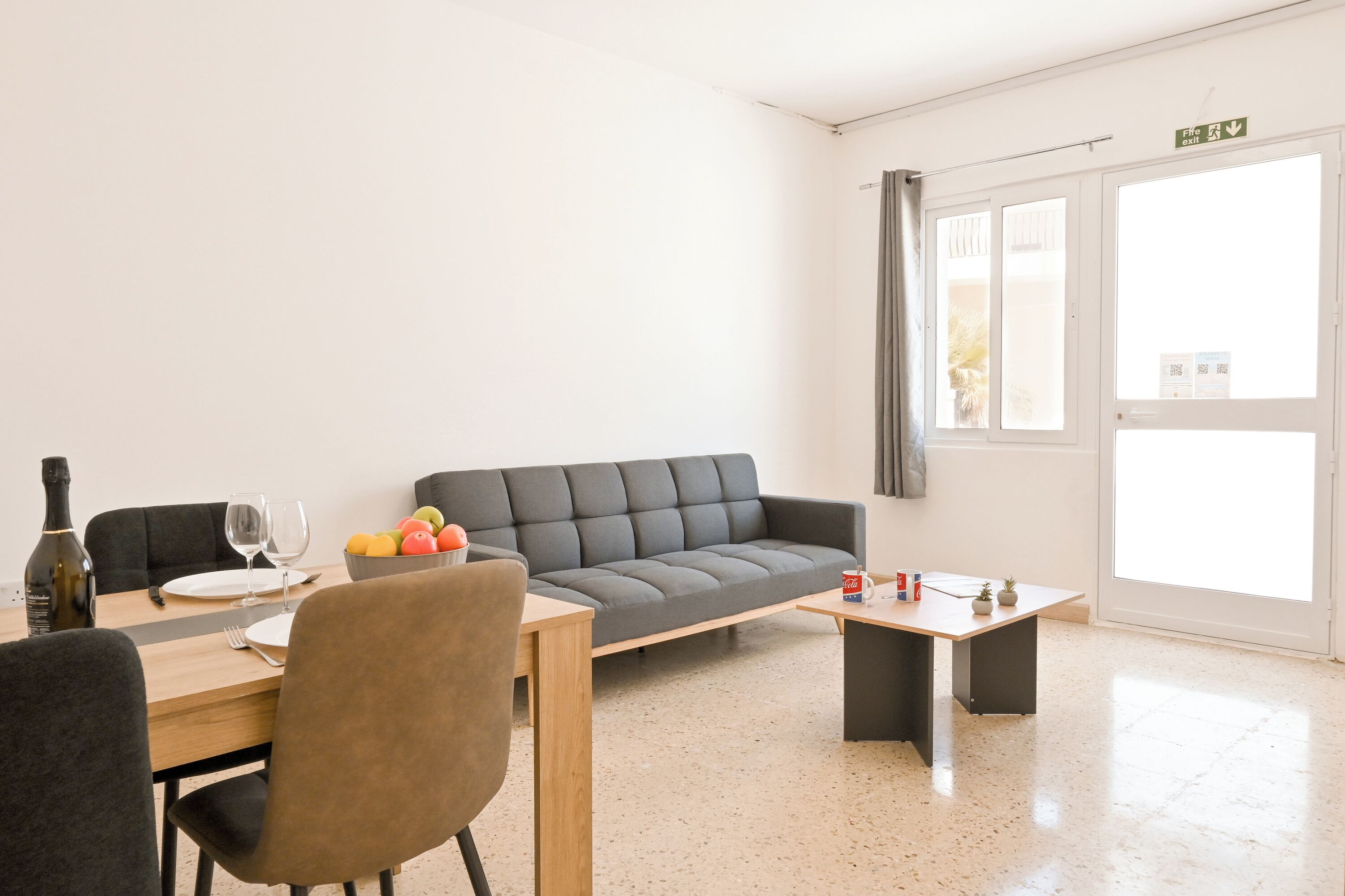 A modern living room with a sofa, a dining table with chairs, a coffee table, and a window with curtains.