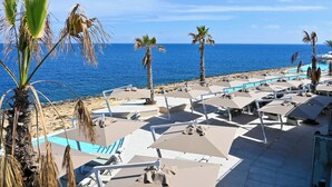 A beachside resort with sun loungers and umbrellas, a pool, and palm trees.