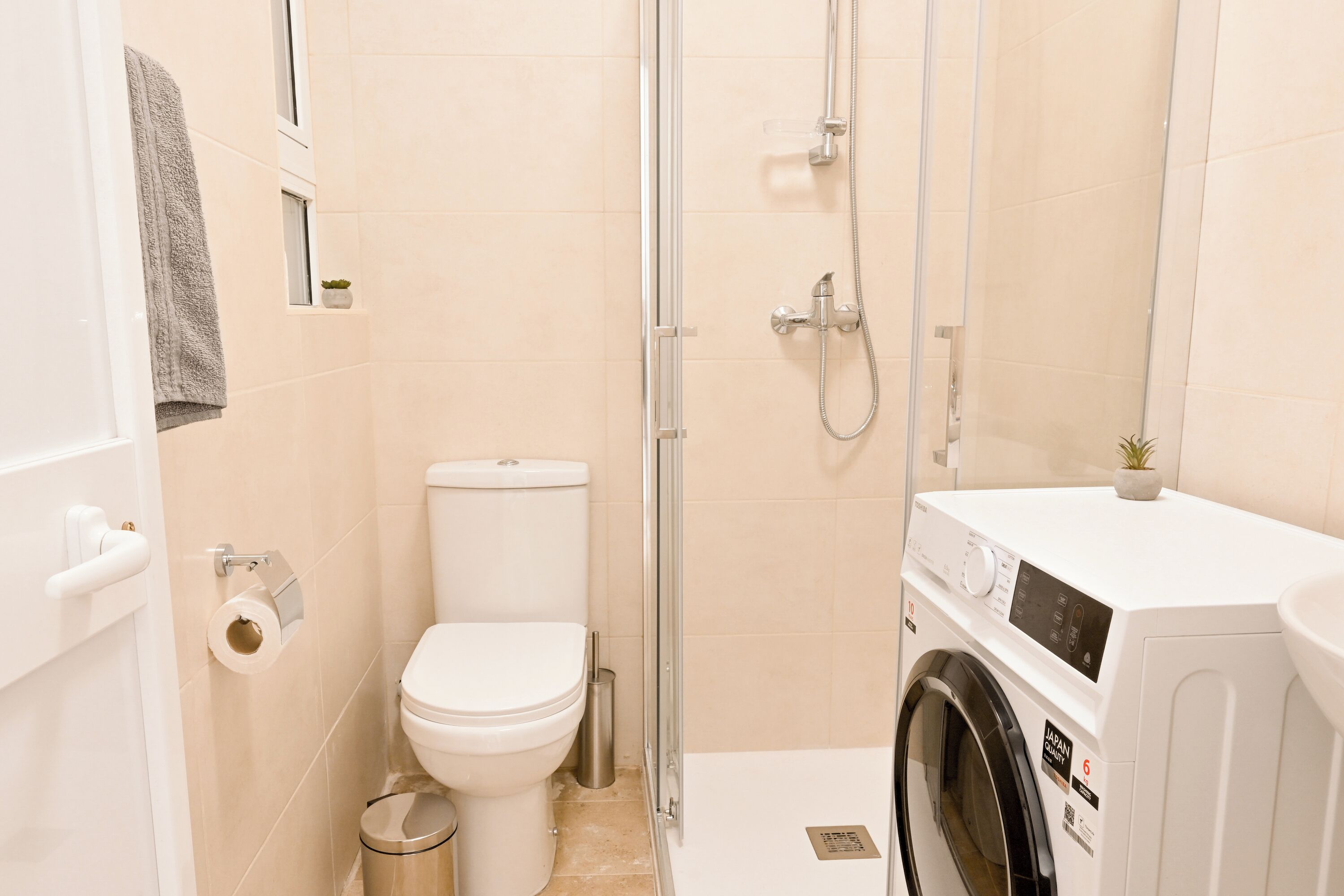 Une petite salle de bain comprenant des toilettes, une douche à parois de verre et un lave-linge à chargement frontal.