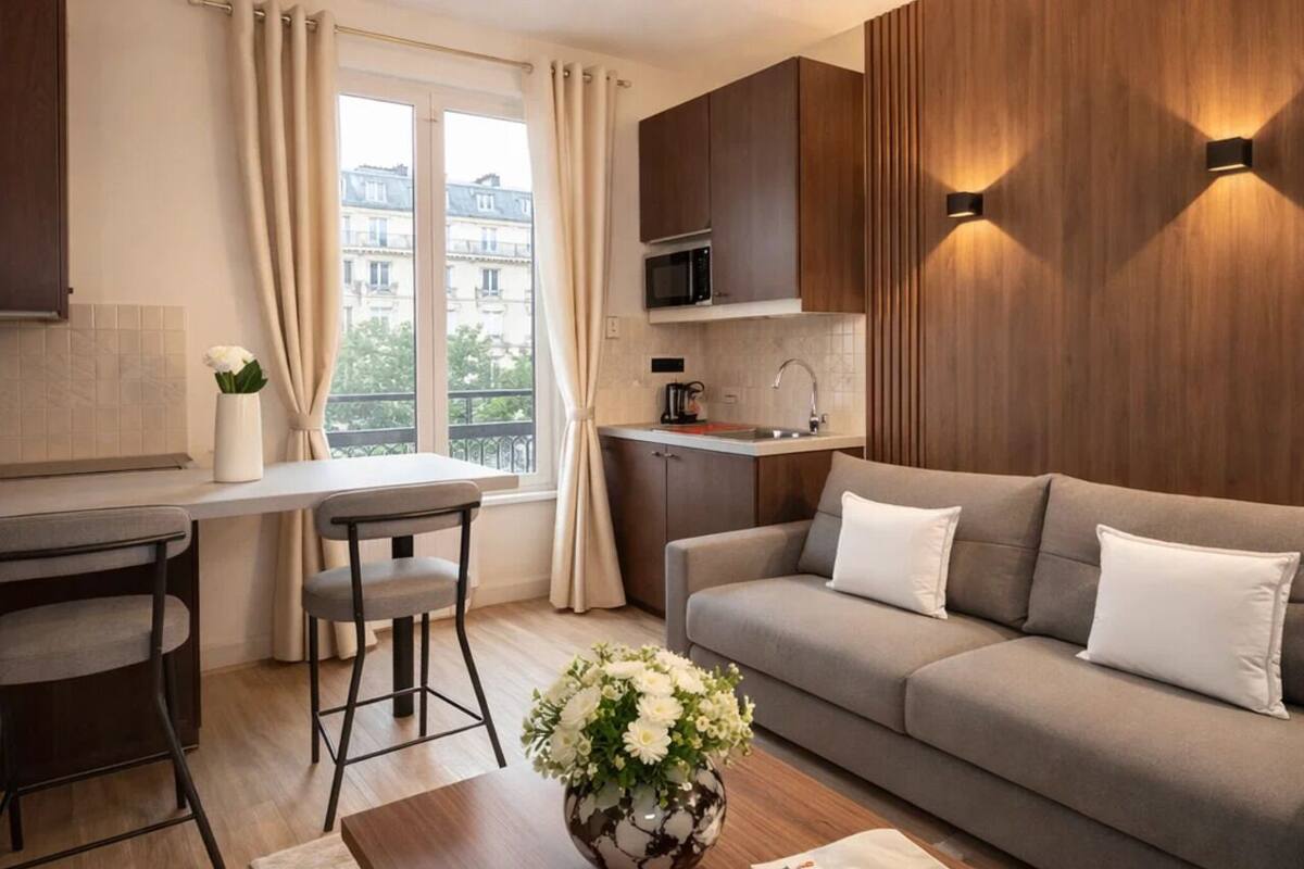 A modern apartment with a dining area, kitchenette, sofa, and a large window.