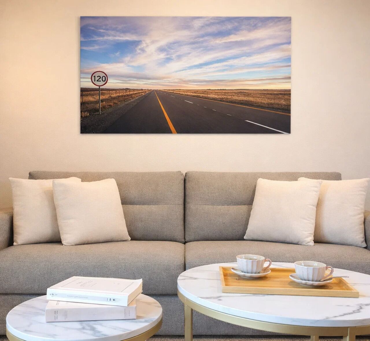 Quarto com sofá, duas mesas redondas, uma mesa de centro e um quadro com uma imagem de estrada.