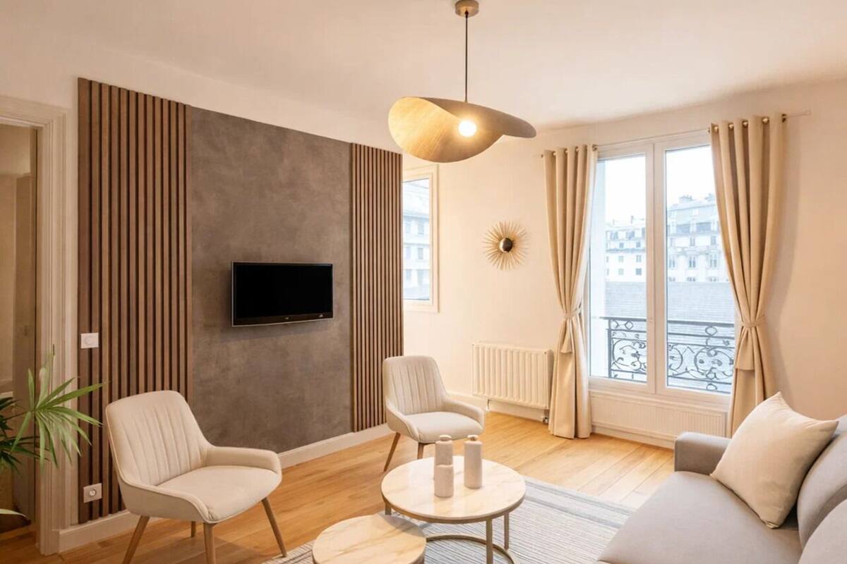 A modern living room with a sofa, two armchairs, a coffee table, and a TV mounted on the wall.