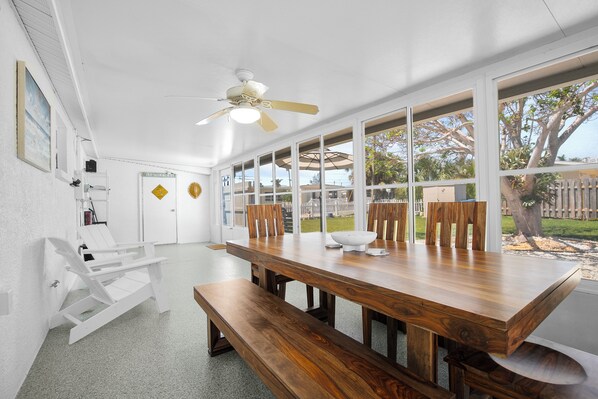 A spacious dining area with a wooden table and benches, large windows offering a view of the outdoors, and a ceiling fan.