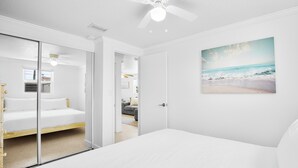 A bedroom with a large bed, a ceiling fan, and a beach-themed wall art.
