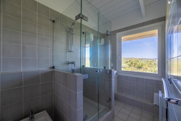 Un baño moderno con ducha envuelta en vidrio, inodoro y ventana con vistas al exterior.