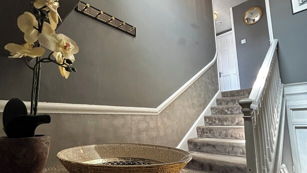 Un intérieur moderne avec un comptoir en marbre, un bol décoratif, une orchidée en pot et un escalier surmonté d’un luminaire.