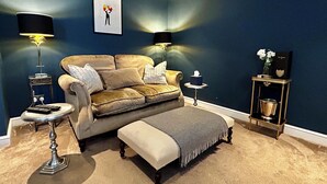 Un salon comprenant un canapé, deux tables d’appoint, une lampe, un tableau accroché au mur et une petite table sur laquelle est posé un vase.