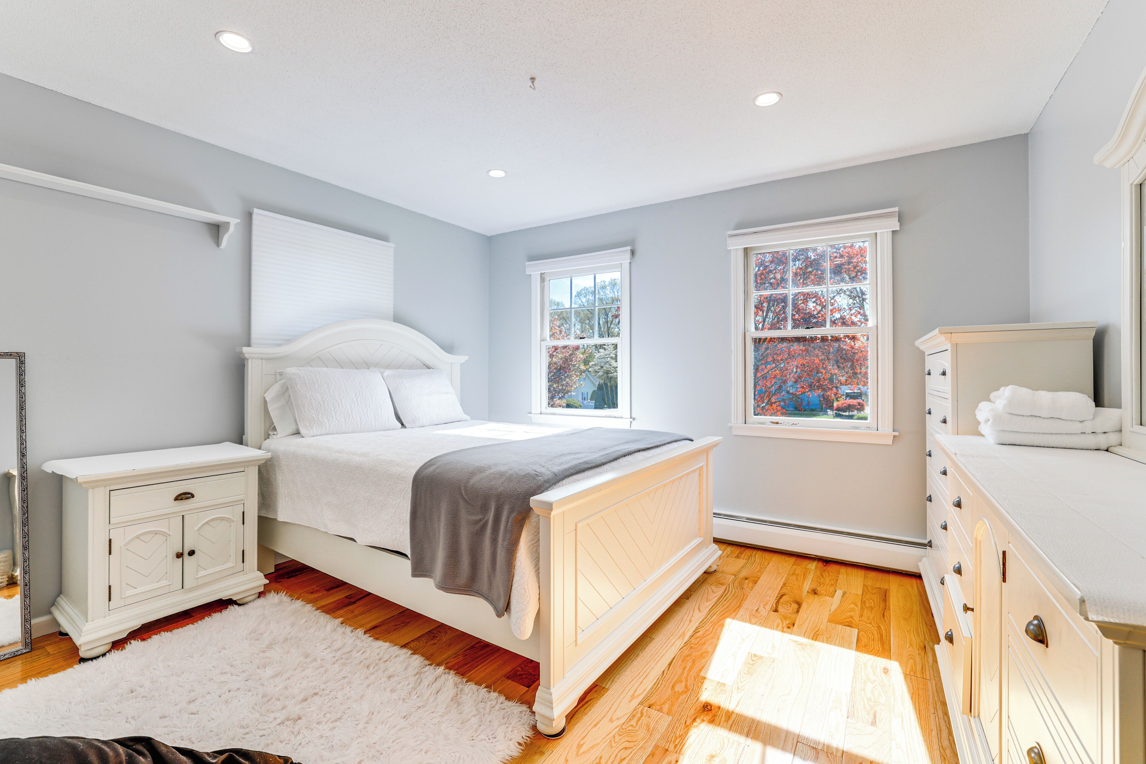 Une chambre à coucher comprenant un lit, une table de chevet, une commode et deux fenêtres.