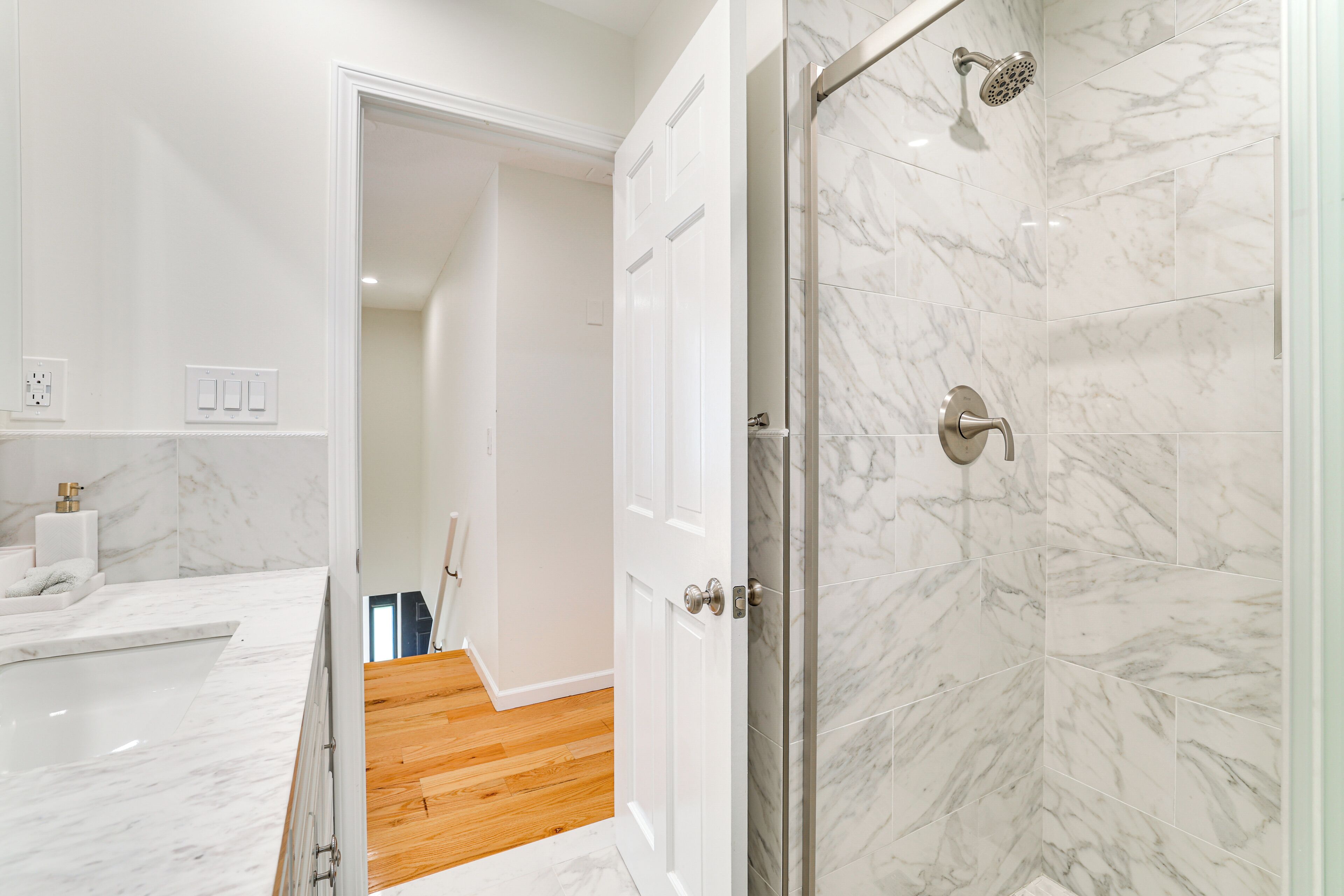 A modern bathroom with a shower, marble tiles, a wooden floor, and a white countertop.