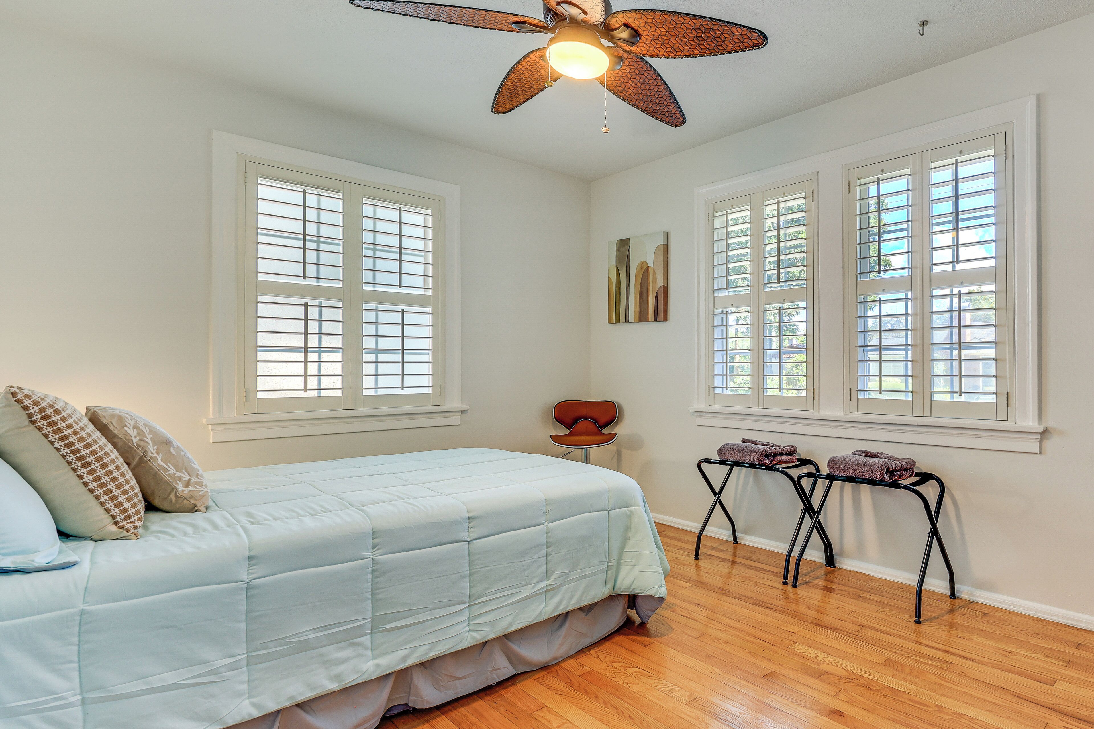 A bedroom with a bed, two windows, a ceiling fan, and a chair.