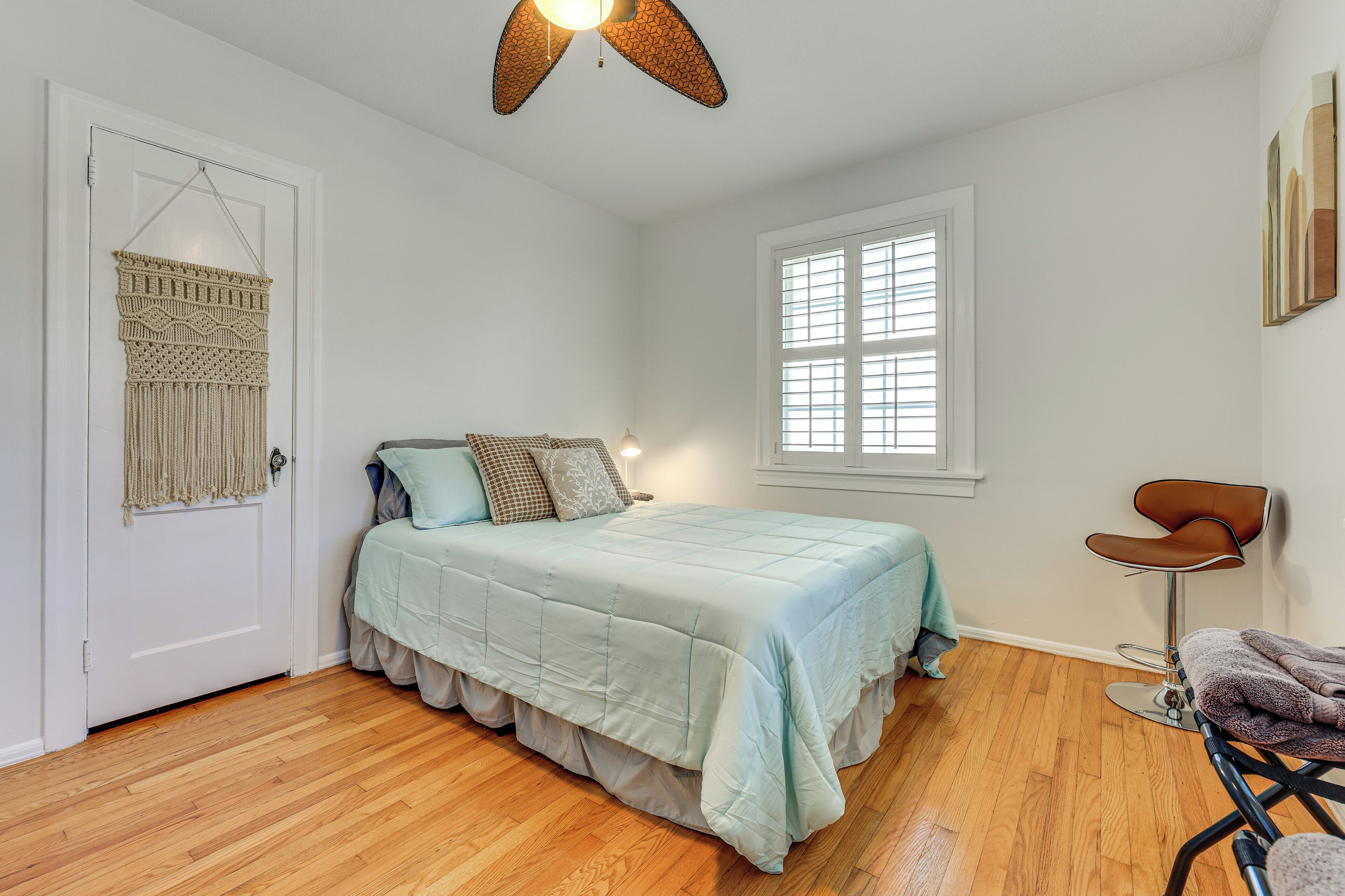 A bedroom with a bed, a chair, a hanging macrame wall decoration, and a window.