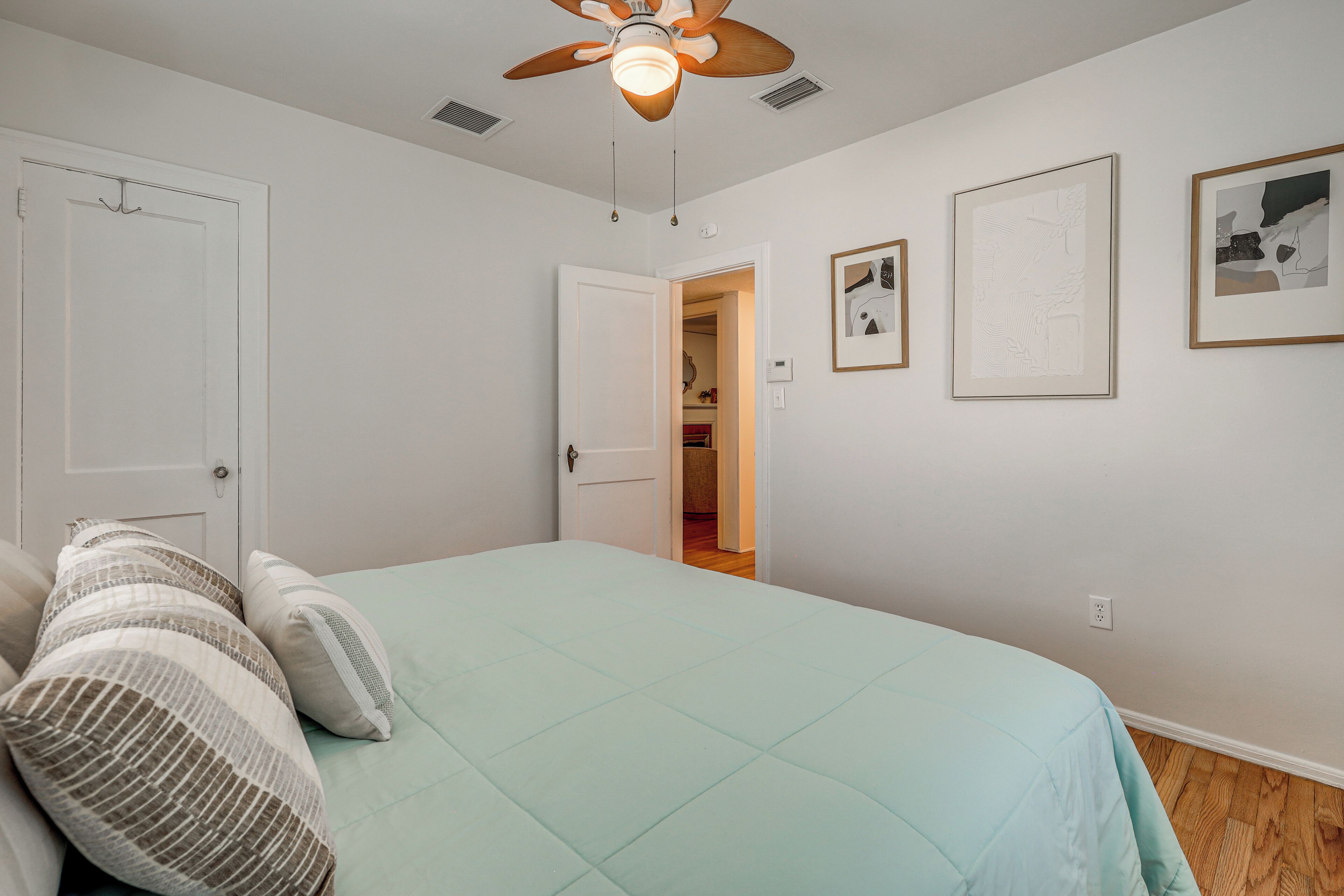 A bedroom with a bed, pillows, a ceiling fan, and framed pictures on the wall.