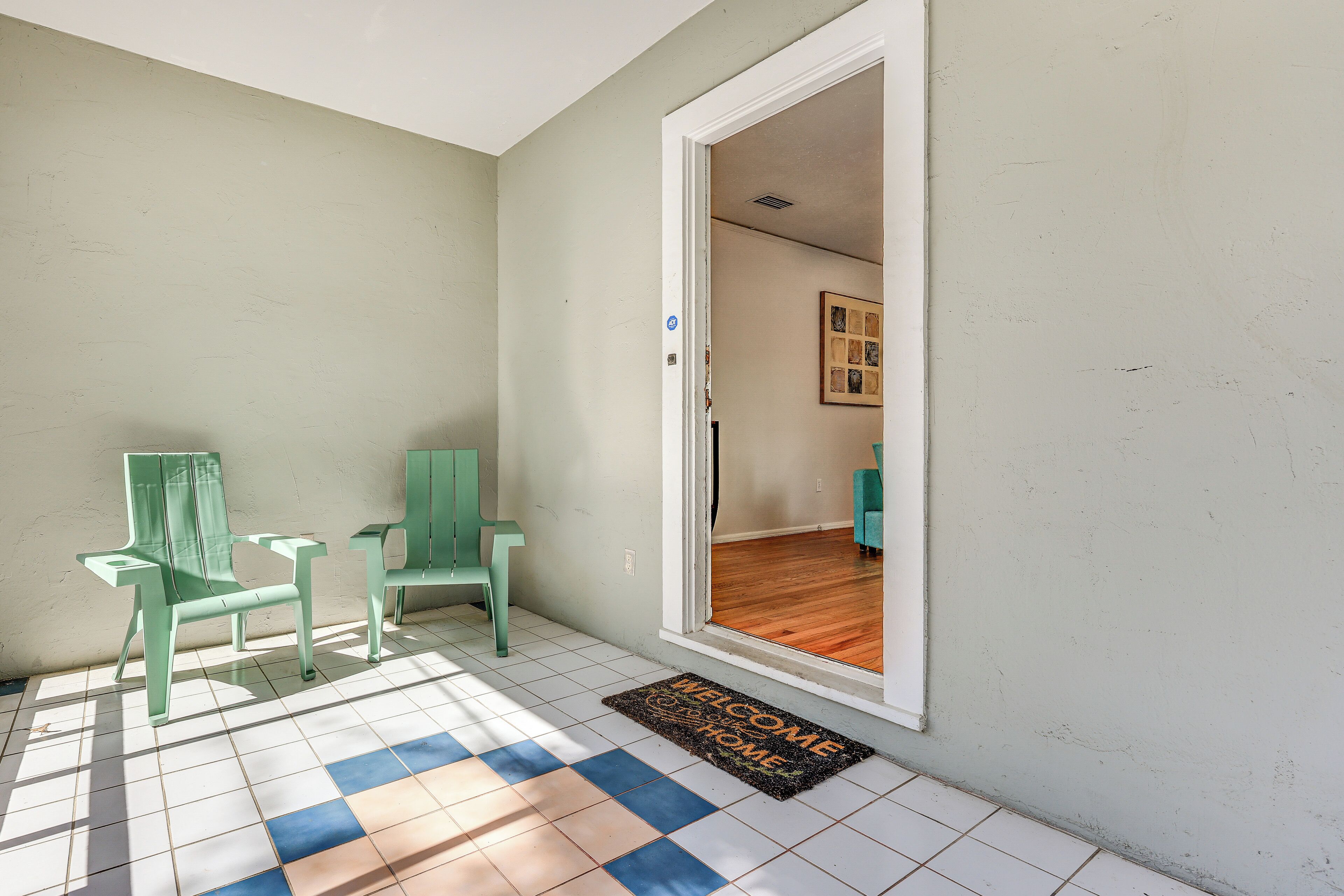 A room with a tiled floor, a welcome mat, and two green chairs.