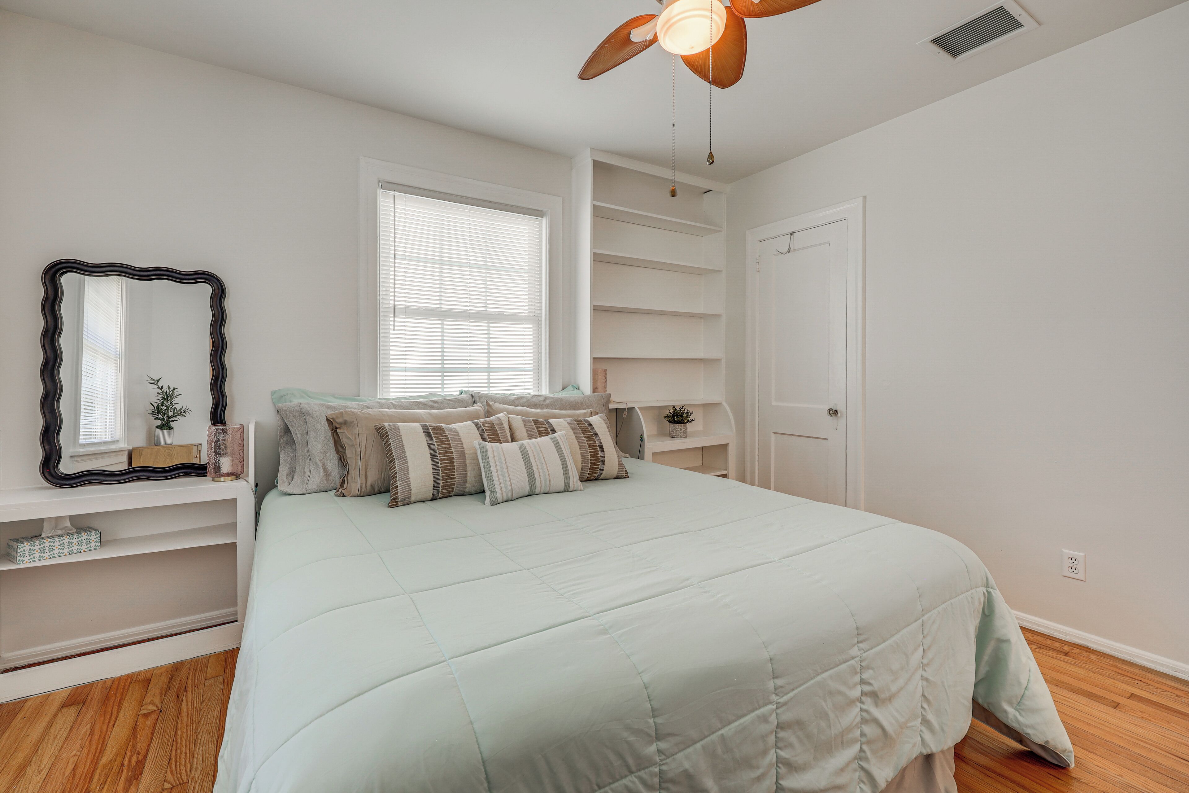 A bedroom with a bed, a ceiling fan, a window, built-in shelves, and a door.