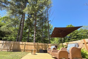 Un patio trasero con una terraza de madera, mobiliario de mimbre y un gran paraguas.