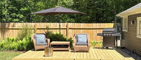 A wooden deck with two wicker chairs, a metal table, and a barbecue grill.