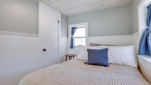 A bedroom with a large bed, a window with curtains, a small wooden stool, and a white door. - Swim, Hike & Unwind: Frankfort Cottage w/ Fire Pit (Frankfort)