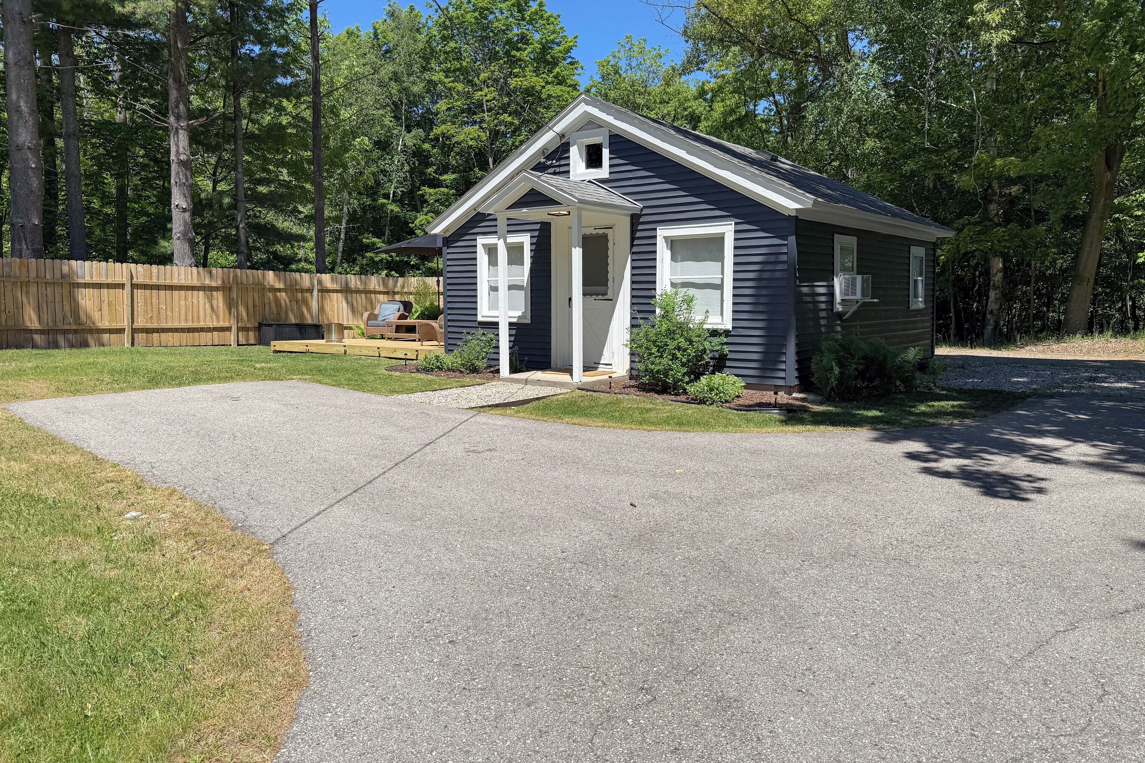 A small single-story house with a front porch, a driveway, and a wooden fence.