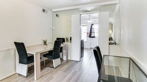 A dining area with a white table and black chairs, a glass partition, and a ceiling fan. - Condo 9 Mi to Dtwn Dallas: BBQ By the Pool! (Dallas)